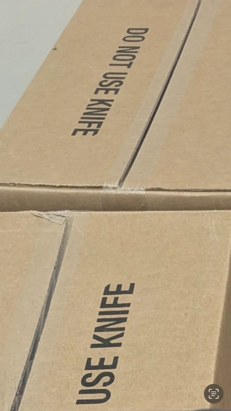 A close-up of two stacked cardboard boxes, each with printed text. The top box reads 'DO NOT USE KNIFE' and the bottom box…