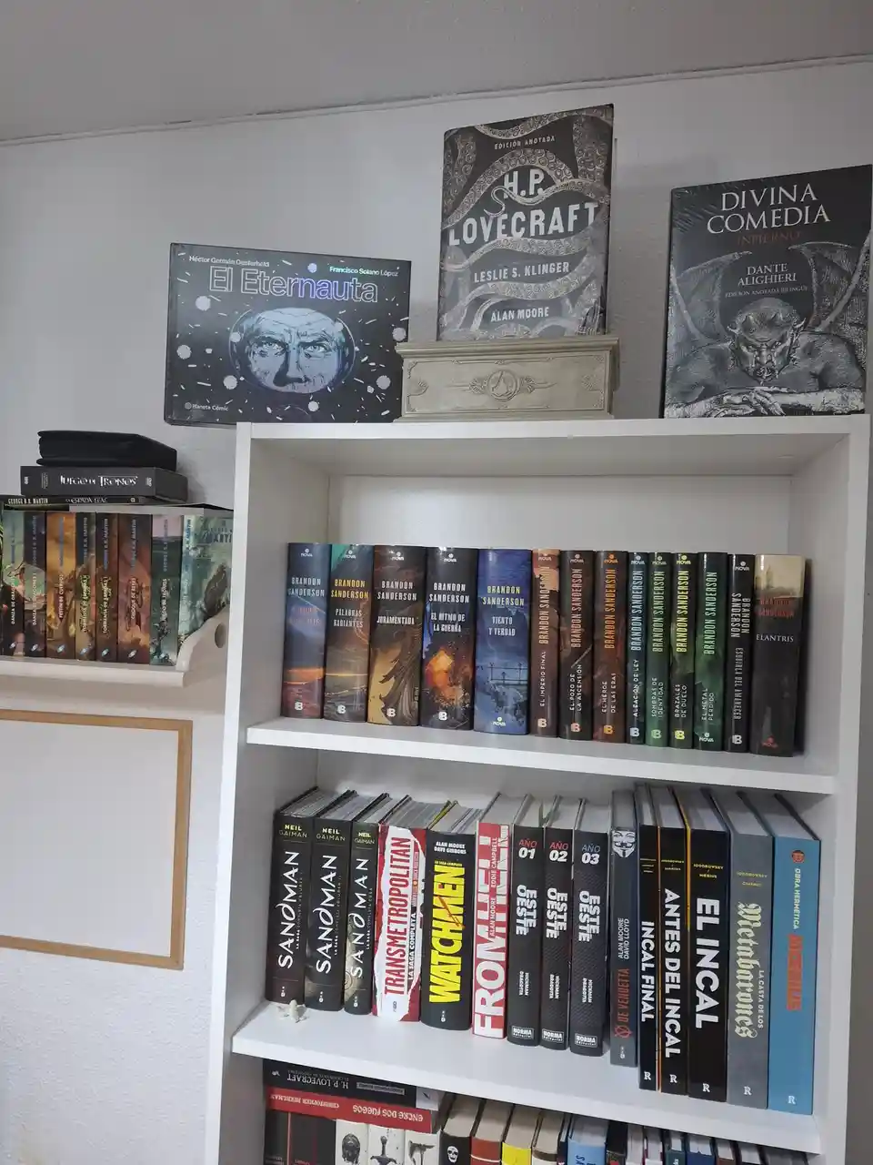 A white bookshelf displays a collection of books, including 'El Eternauta', 'H.P. Lovecraft', and 'Divina Comedia' on the…