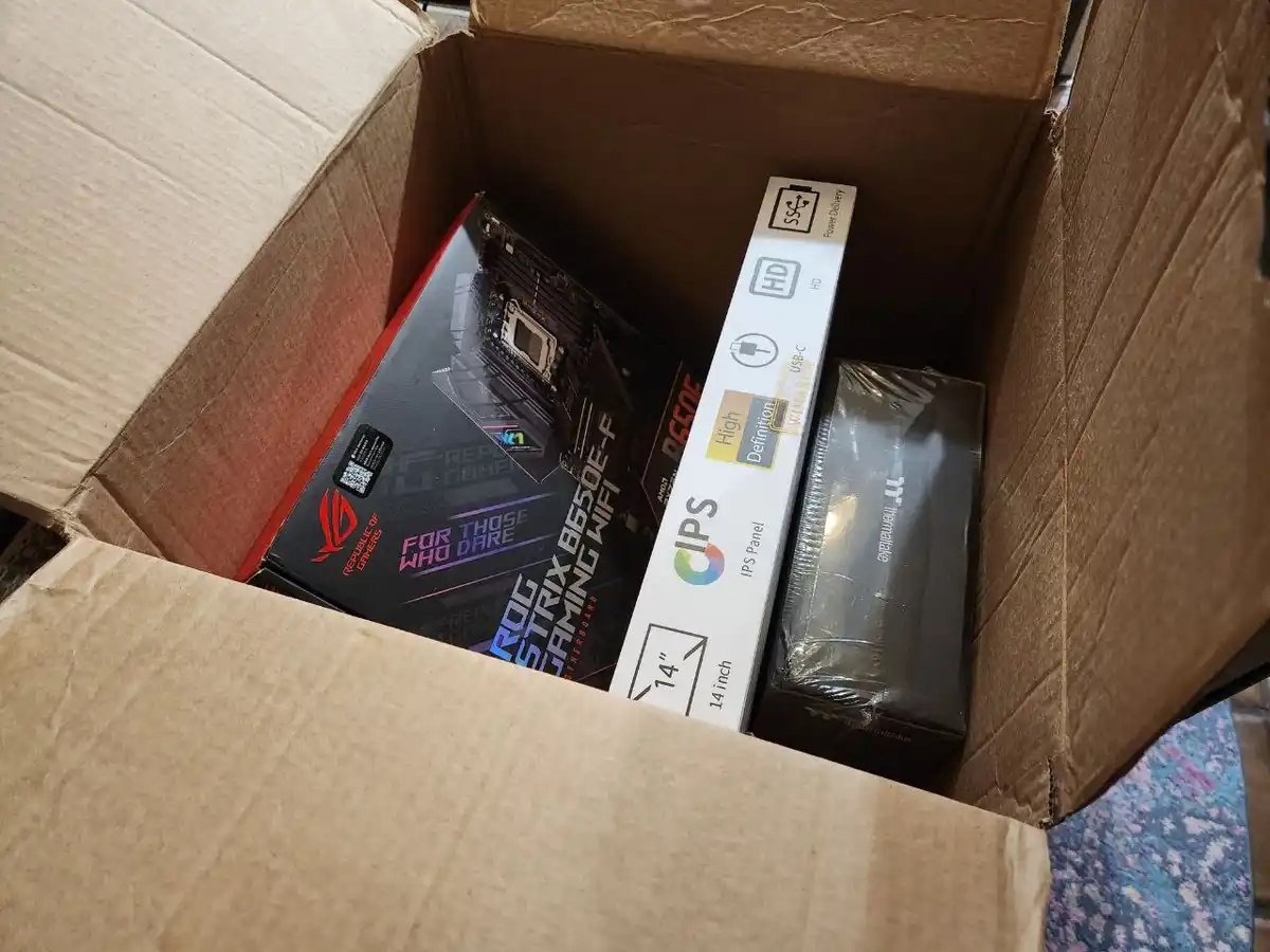 An open cardboard box contains three tech product boxes: an ASUS ROG Strix B650E-F gaming motherboard box with 'FOR THOSE…