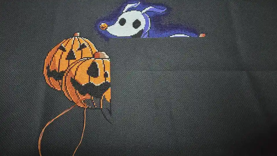 A close-up of a dark gray fabric with a cross-stitch pattern depicting Jack Skellington from The Nightmare Before Christmas…