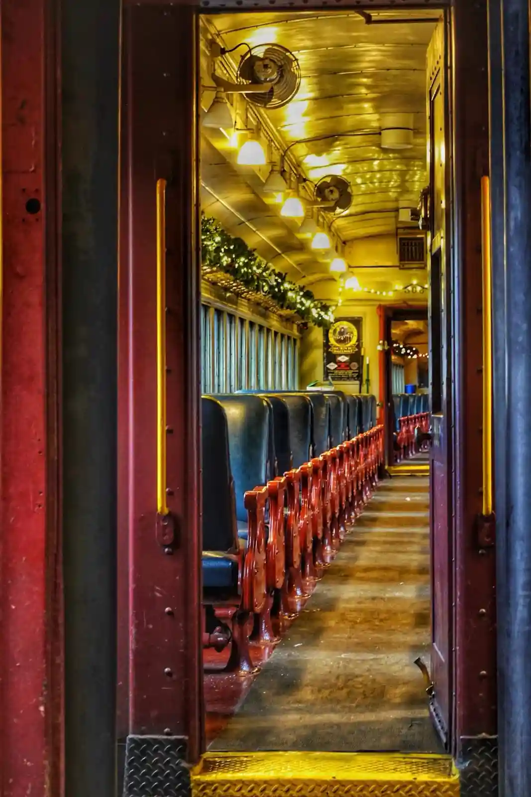 A view from the doorway of an old train car, showing rows of empty blue seats with red armrests, a yellow step, and warm…