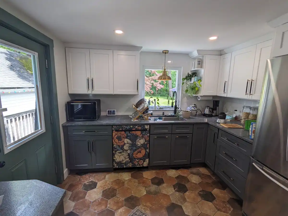A modern kitchen with white upper cabinets and dark gray lower cabinets, one of which is covered in a colorful floral…