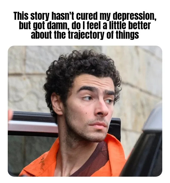 A man with curly dark hair and stubble, wearing an orange jumpsuit, looks off to the side with a slightly skeptical or…