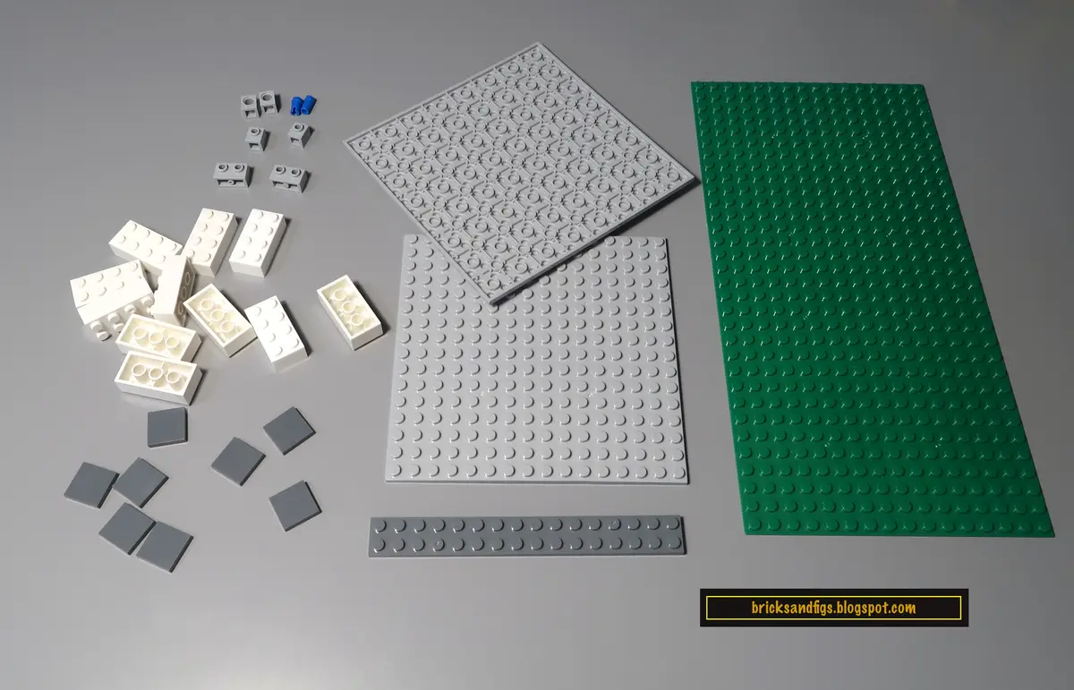 An overhead shot of various Lego baseplates and bricks arranged on a gray surface, including gray, green, and white pieces…
