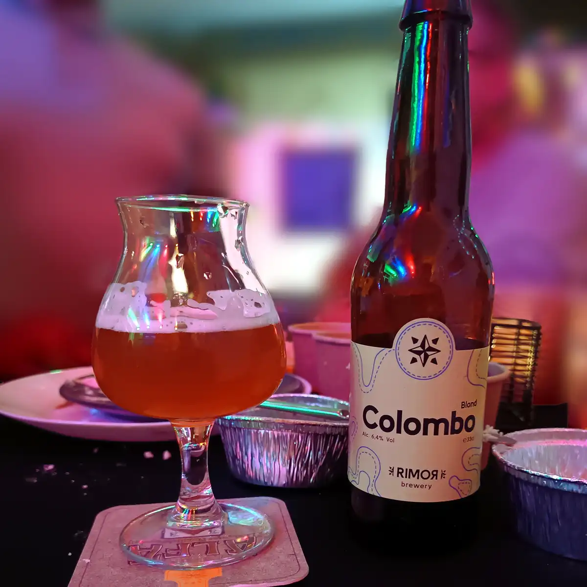 A close-up photo shows a bottle of 'Colombo' beer from Rimor Brewery next to a tulip-shaped glass filled with amber beer and…