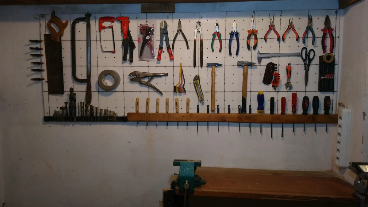 A well-organized workshop wall displays an extensive array of tools including hammers, pliers, screwdrivers, saws, and drill…