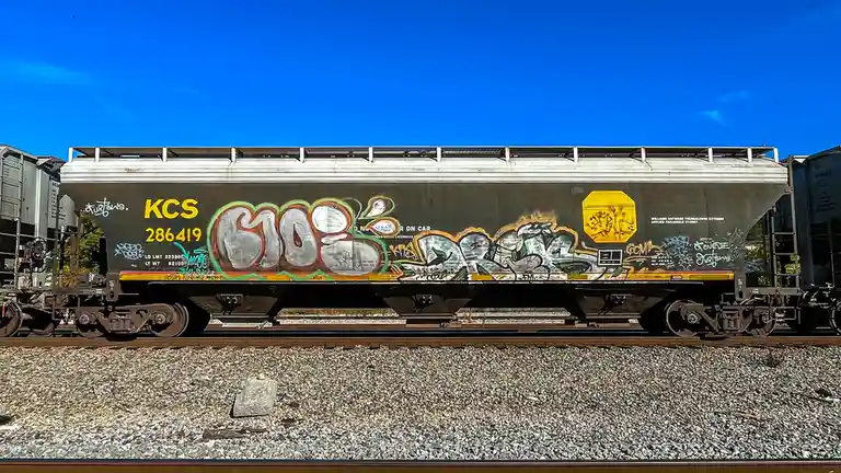 A side view of a dark gray KCS (Kansas City Southern) freight train car, number 286419, covered in colorful graffiti tags…