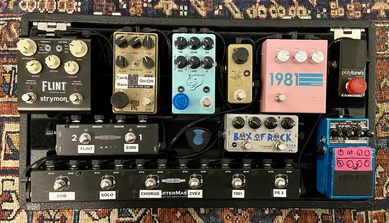An overhead shot of a densely packed guitar pedalboard filled with various effects pedals from brands like Strymon, TC…