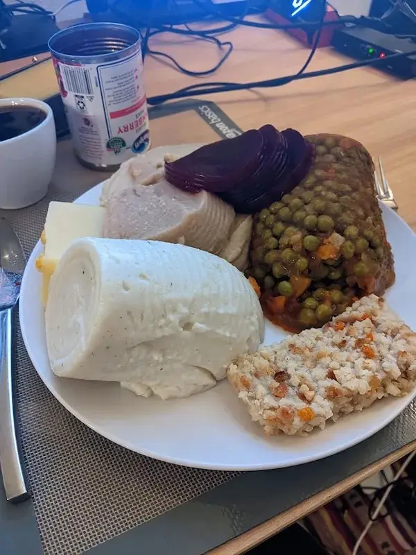 A plate of food featuring a large portion of mashed potatoes, sliced turkey, peas and carrots, a slice of beetroot, and a…