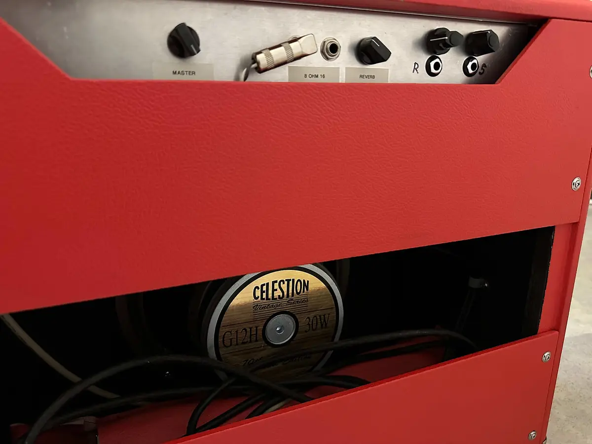A close-up of a red guitar amplifier showing its control knobs labeled 'MASTER', '8 OHM 16', and 'REVERB' on a silver panel…