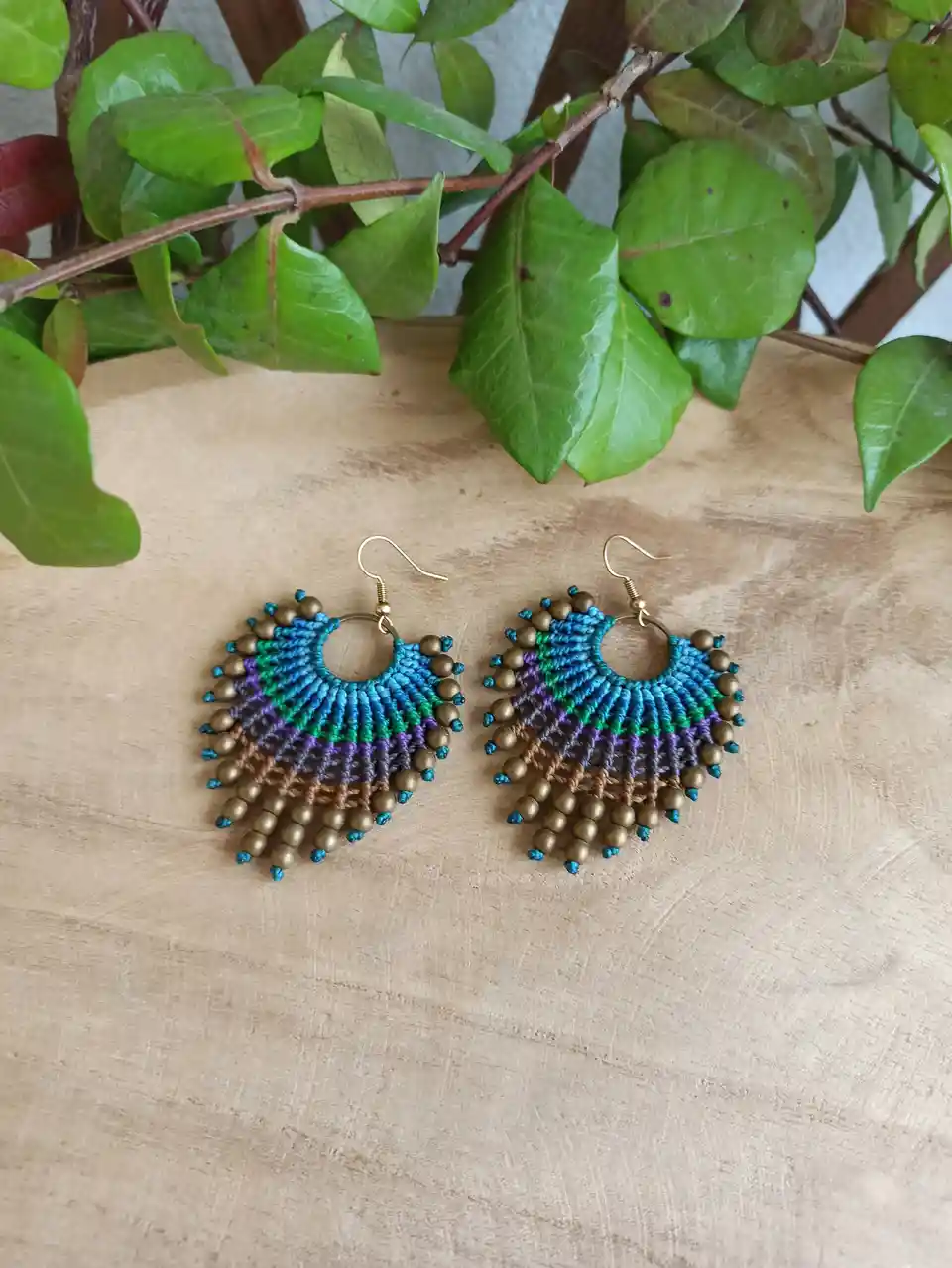A pair of handmade, colorful beaded earrings with gold hooks, featuring a fan-like design with blue, green, purple, and gold…
