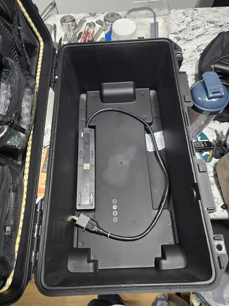 An open, black, rugged-looking case sits on a kitchen counter, its interior mostly empty except for a single power cord…