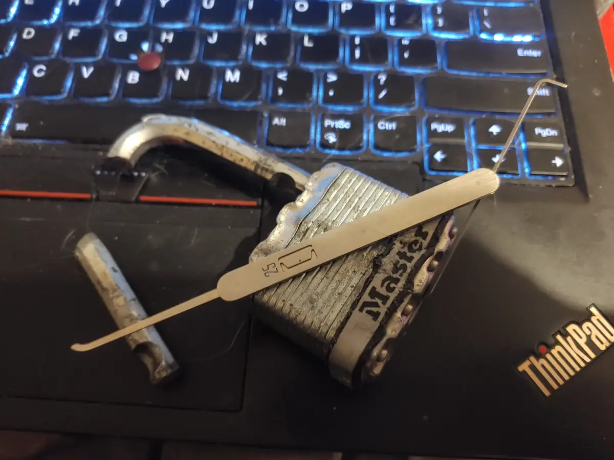 A close-up photo shows a Master brand padlock lying on a black Lenovo ThinkPad laptop keyboard, with its shackle open. Two…