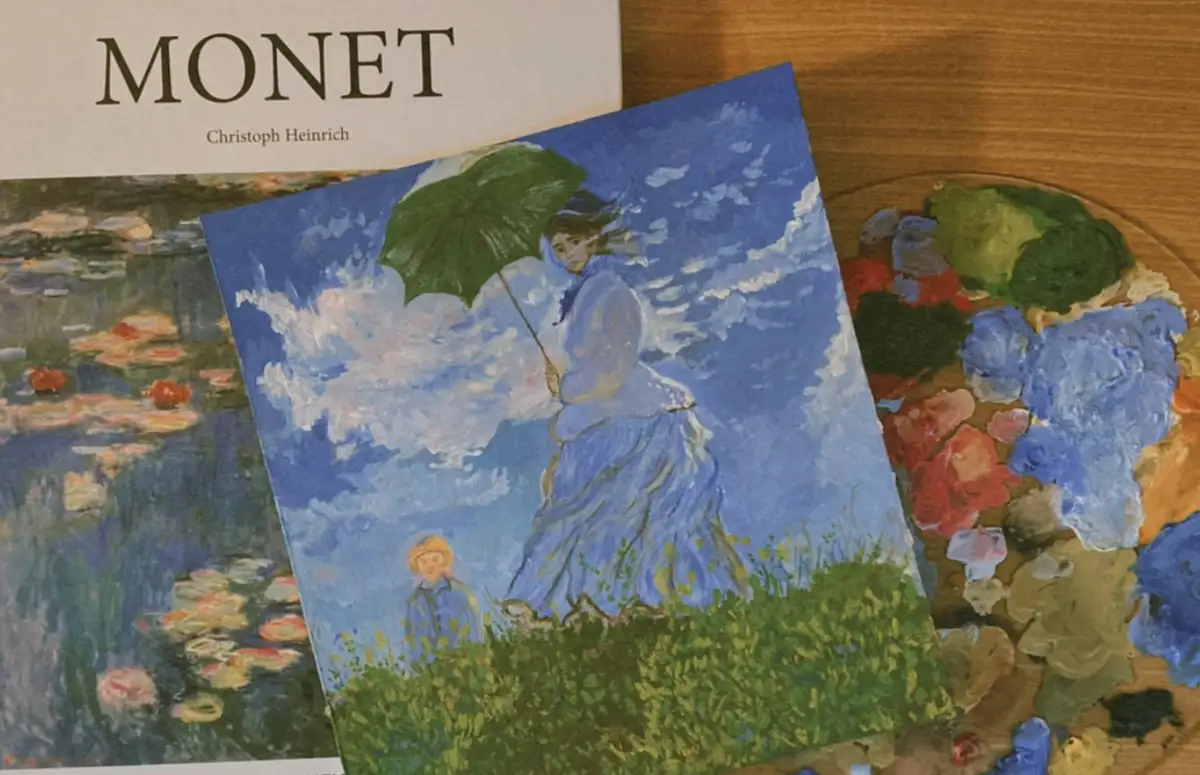 A photograph shows a book titled 'MONET' by Christoph Heinrich, a small painting of a woman in a blue dress holding a green…