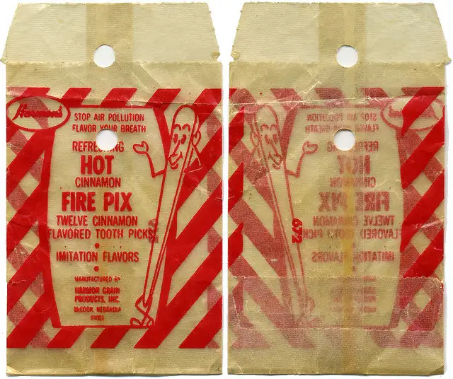 Two vintage, weathered paper packages of 'Fire Pix' cinnamon-flavored toothpicks are shown side-by-side. The red and beige…