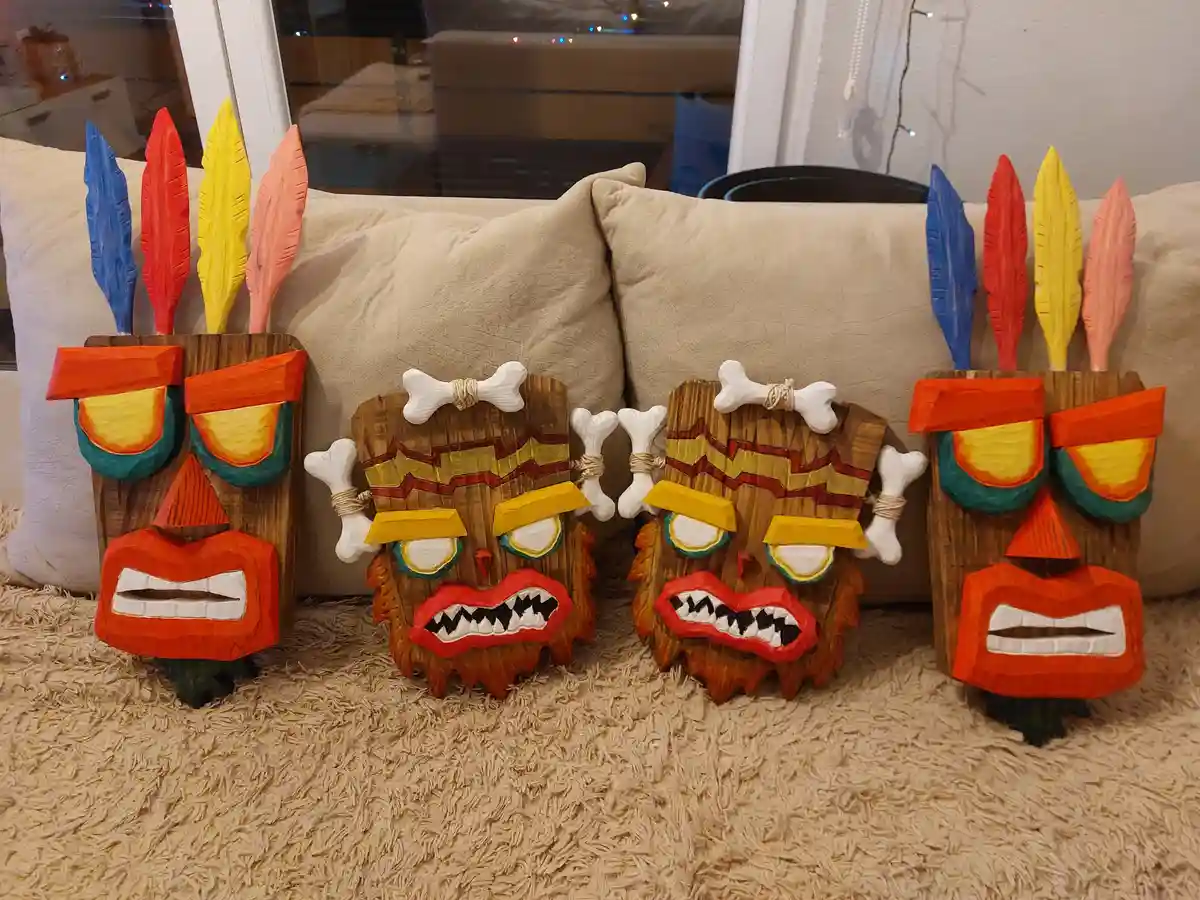 Four hand-carved wooden masks resembling characters from the video game 'Crash Bandicoot' are arranged on a carpeted floor…