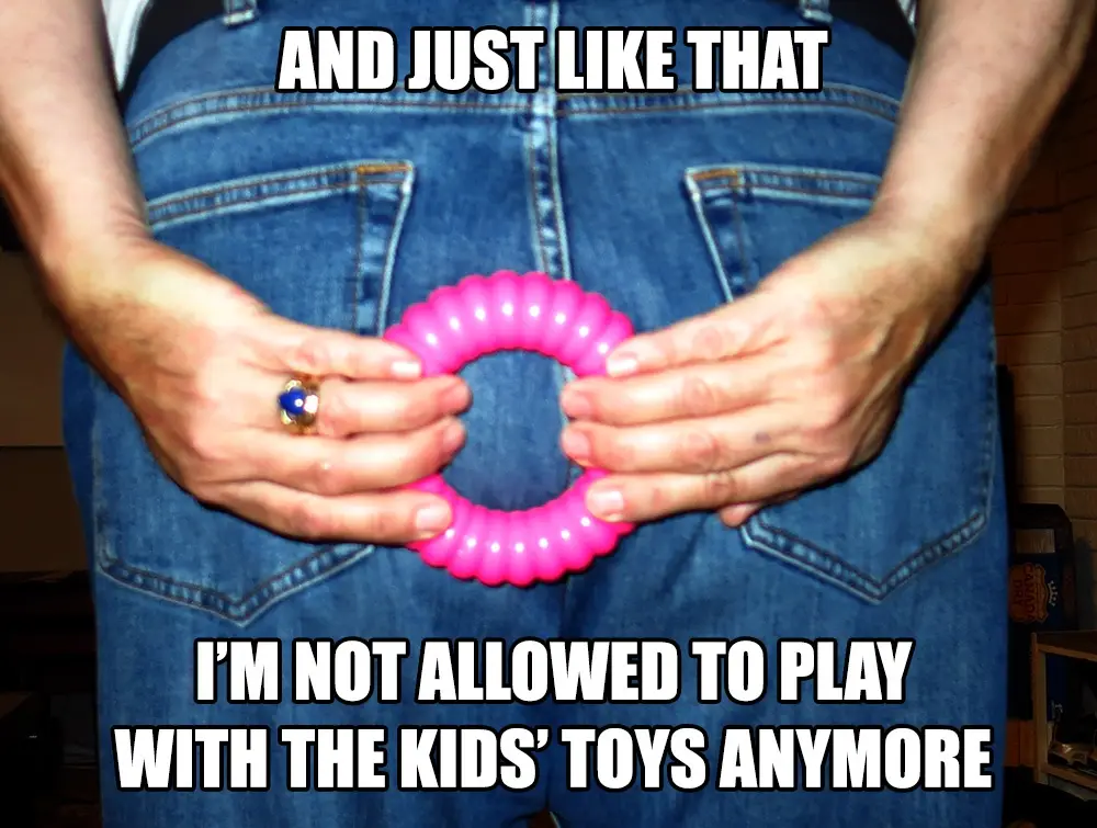 A person wearing blue jeans holds a bright pink, segmented plastic ring toy with both hands, positioned at waist level. The…