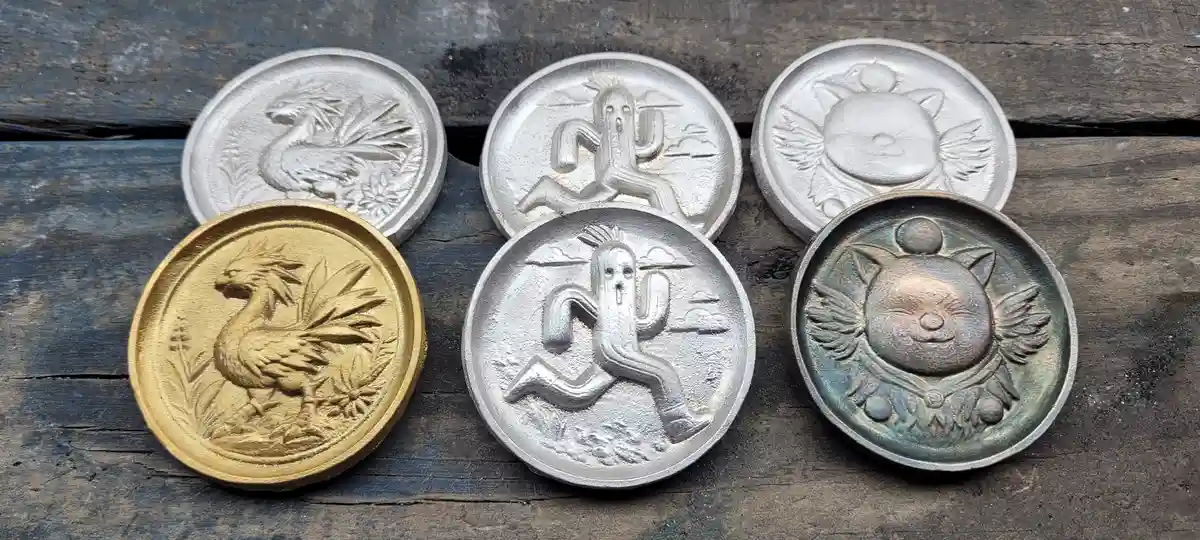Five handcrafted, circular metal coins with raised relief designs lie on a weathered wooden surface. One coin is gold and…