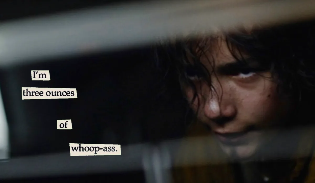 A close-up shot of a young man with dark, wet-looking hair looking intensely forward, partially obscured by a horizontal…