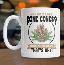 A white ceramic coffee mug with a handle on the left sits on a wooden surface. The mug features a graphic of a pine cone…