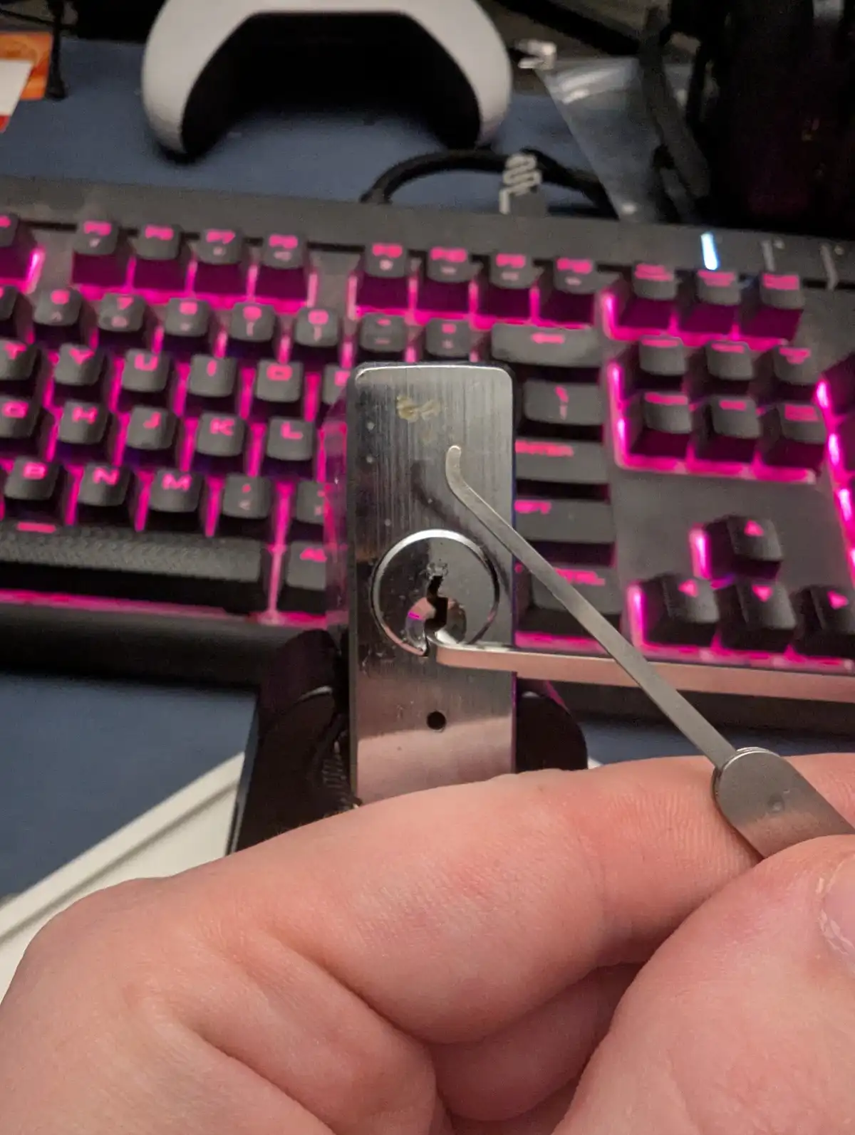 A close-up photo shows a hand using a lock-picking tool to manipulate a small, metallic lock that has been attached to a…