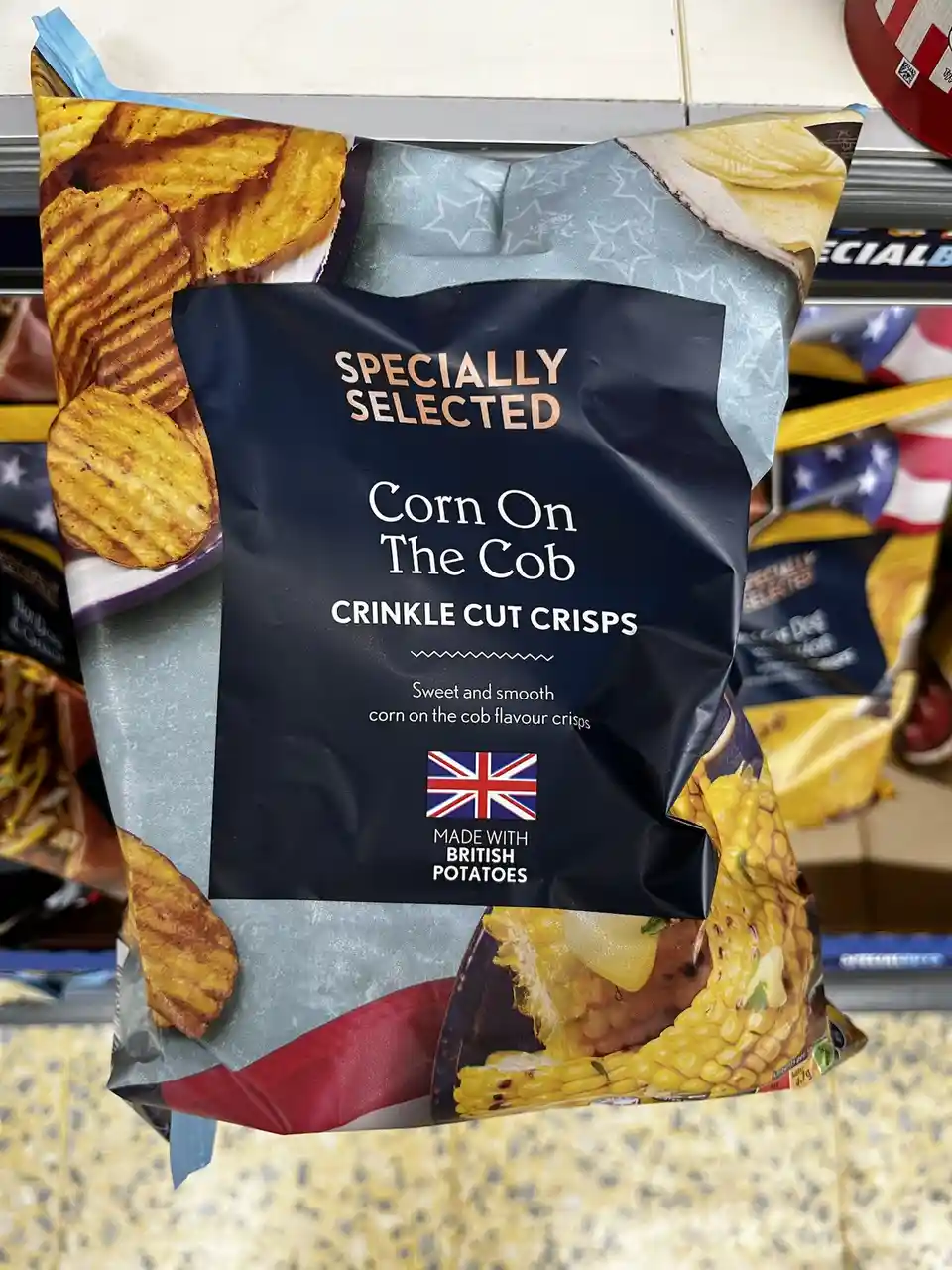 A bag of crisps labeled 'Specially Selected Corn On The Cob Crinkle Cut Crisps' with text describing 'Sweet and smooth corn…