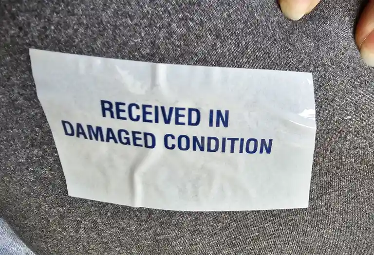 A close-up photo shows a white, slightly crumpled sticker with blue text reading 'RECEIVED IN DAMAGED CONDITION' stuck onto…