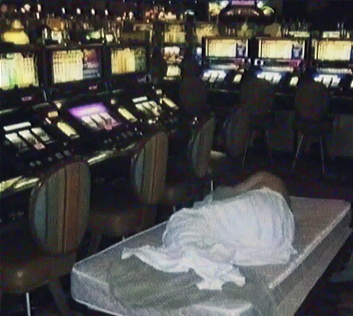 A blurry, low-resolution photo shows a person lying face-down on a mattress placed in the middle of a casino floor…