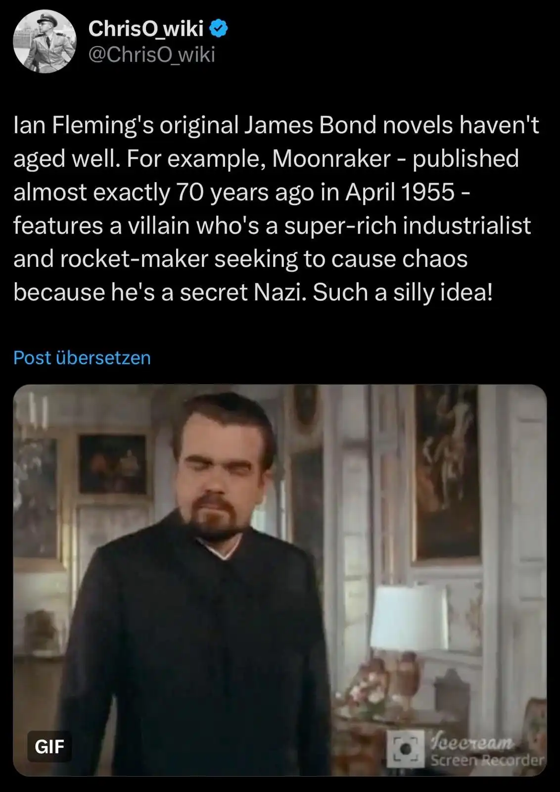 A still image from a James Bond film shows a man with a stern, unimpressed expression, looking directly at the camera. The…
