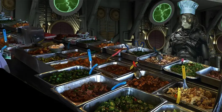 A robot wearing a chef's hat stands behind a long buffet line filled with metal trays of various cooked foods, each with a…