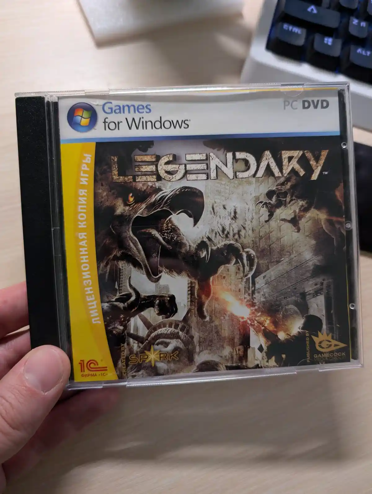 A hand holds a PC DVD game case for 'Legendary', featuring a gritty cover with monsters and a soldier. The spine has Russian…