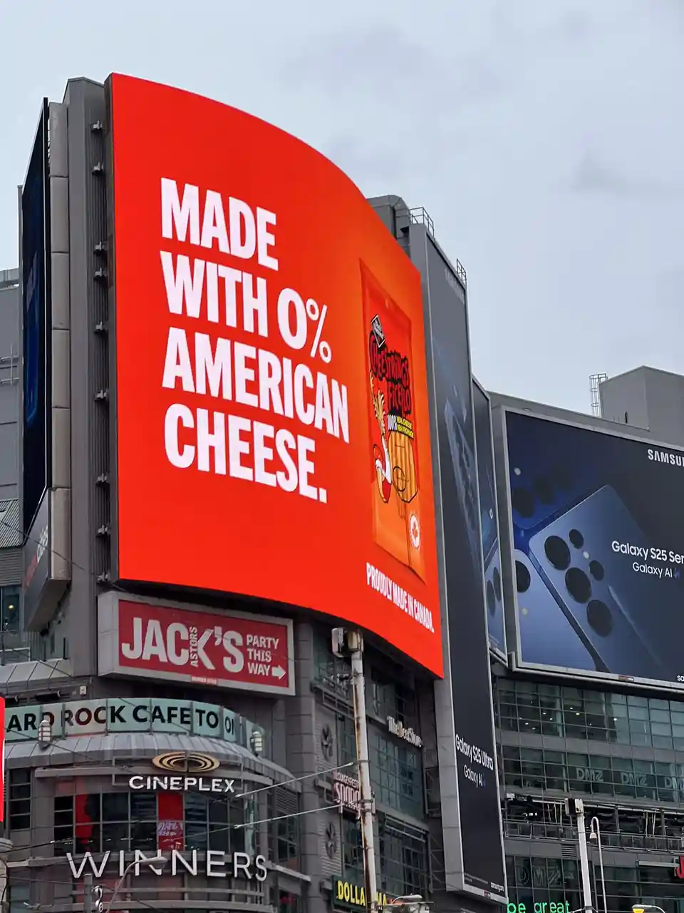 A large red billboard in a city displays the text 'MADE WITH 0% AMERICAN CHEESE.' alongside an image of a Cheez Whiz bag and…