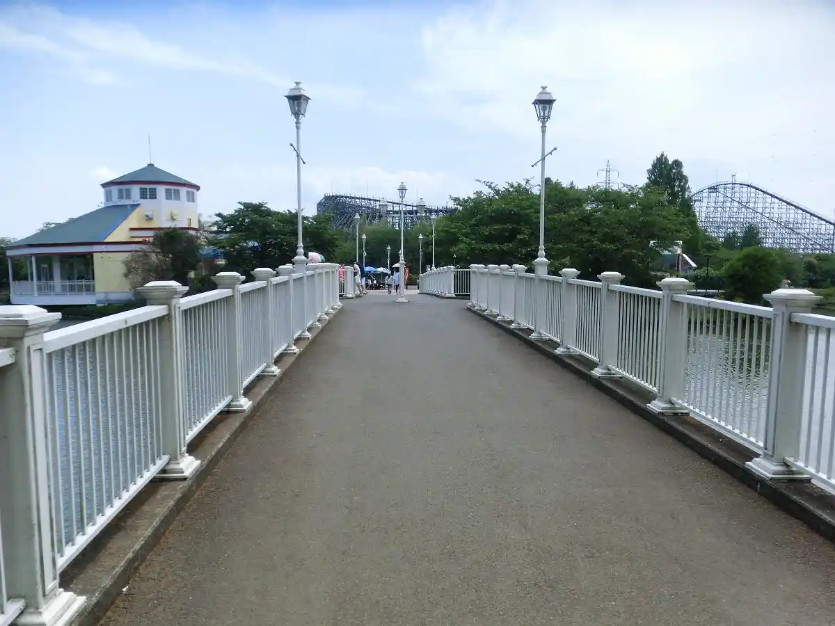 A long, straight pedestrian bridge with white railings and lampposts stretches into the distance, flanked by water. In the…
