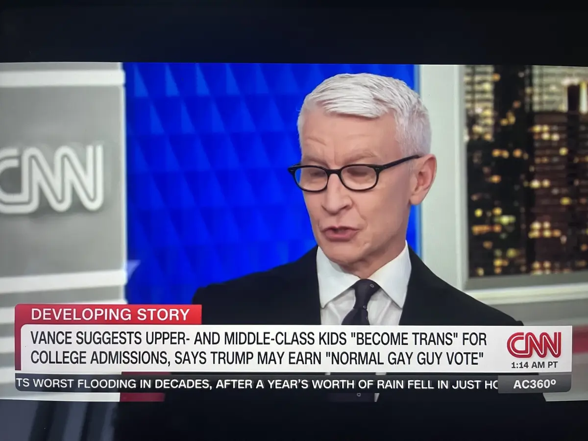 A screenshot of CNN anchor Anderson Cooper looking downcast and serious during a news broadcast. The on-screen text reads…