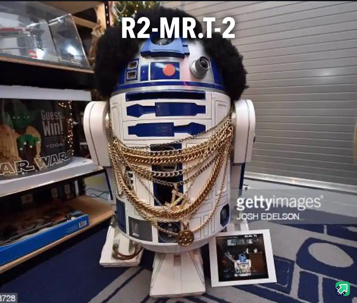 A Star Wars R2-D2 droid model is heavily modified with a large black afro wig and multiple thick gold chains draped around…