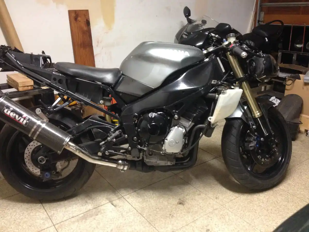 A partially disassembled Yamaha motorcycle sits in a garage, missing its front fairing and rear fender, revealing its engine…
