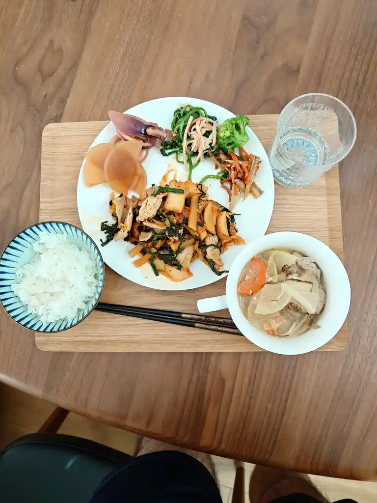 An overhead shot of a wooden table with a meal set on a wooden tray, including a large plate with stir-fried chicken, squid…