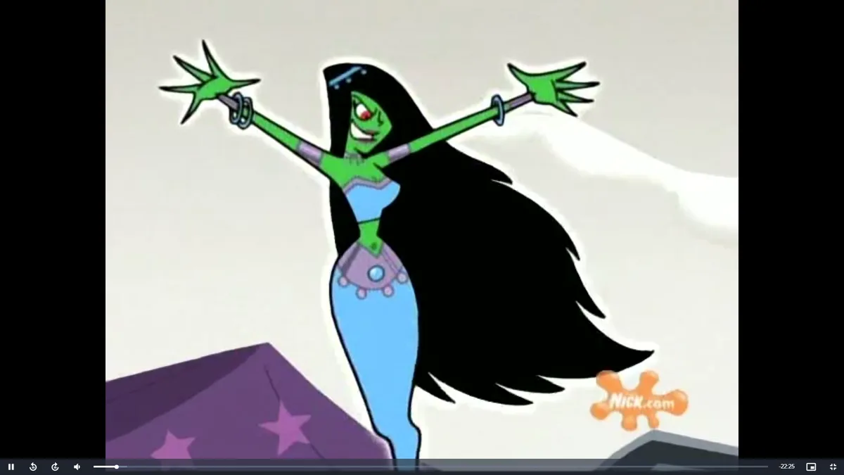 A green-skinned animated character with long black hair, wearing a blue and purple outfit, stands with arms outstretched…
