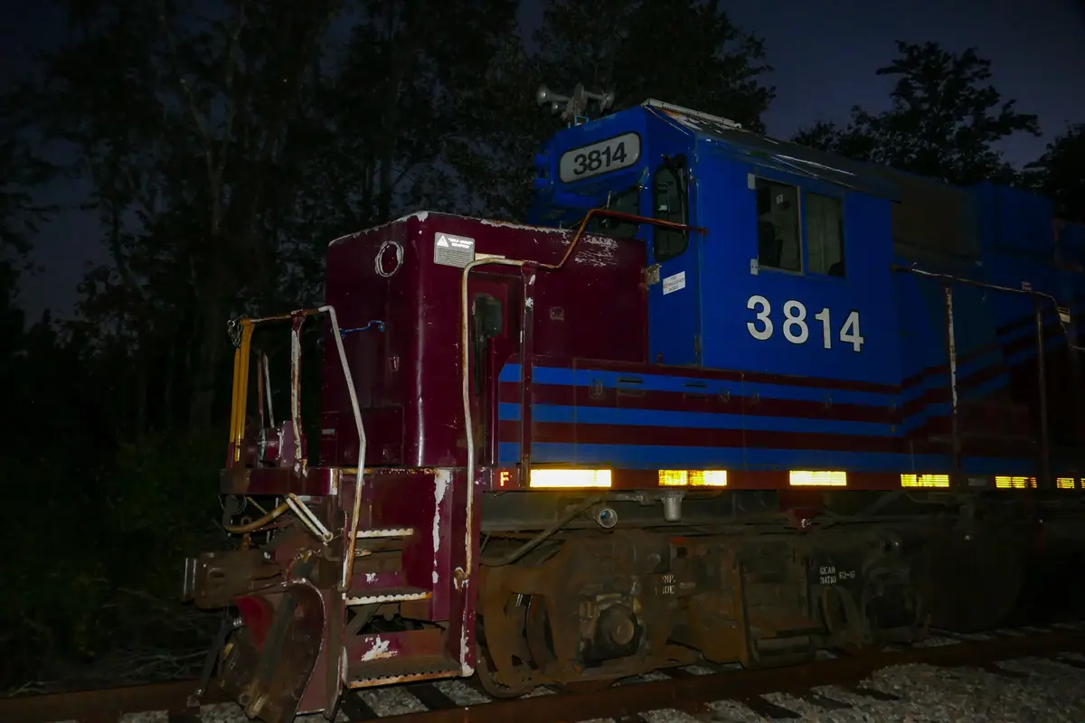 A blue and maroon locomotive, numbered 3814, is shown at night on railway tracks with trees in the background. The number…