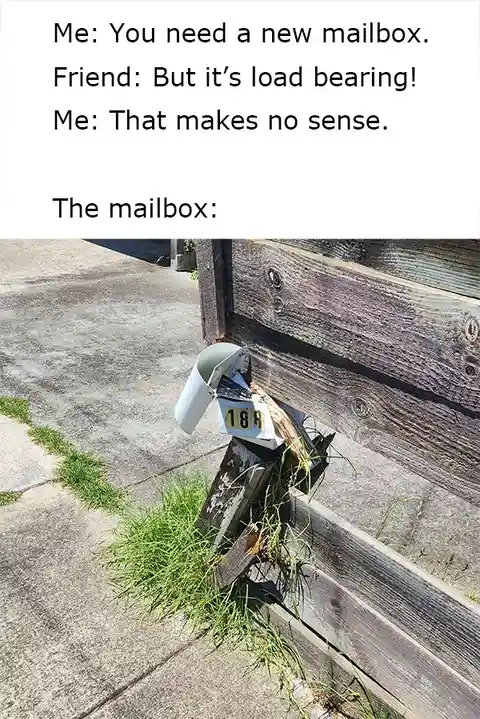 A damaged, broken mailbox is shown attached to a wooden fence post, with grass growing around its base. The mailbox is…