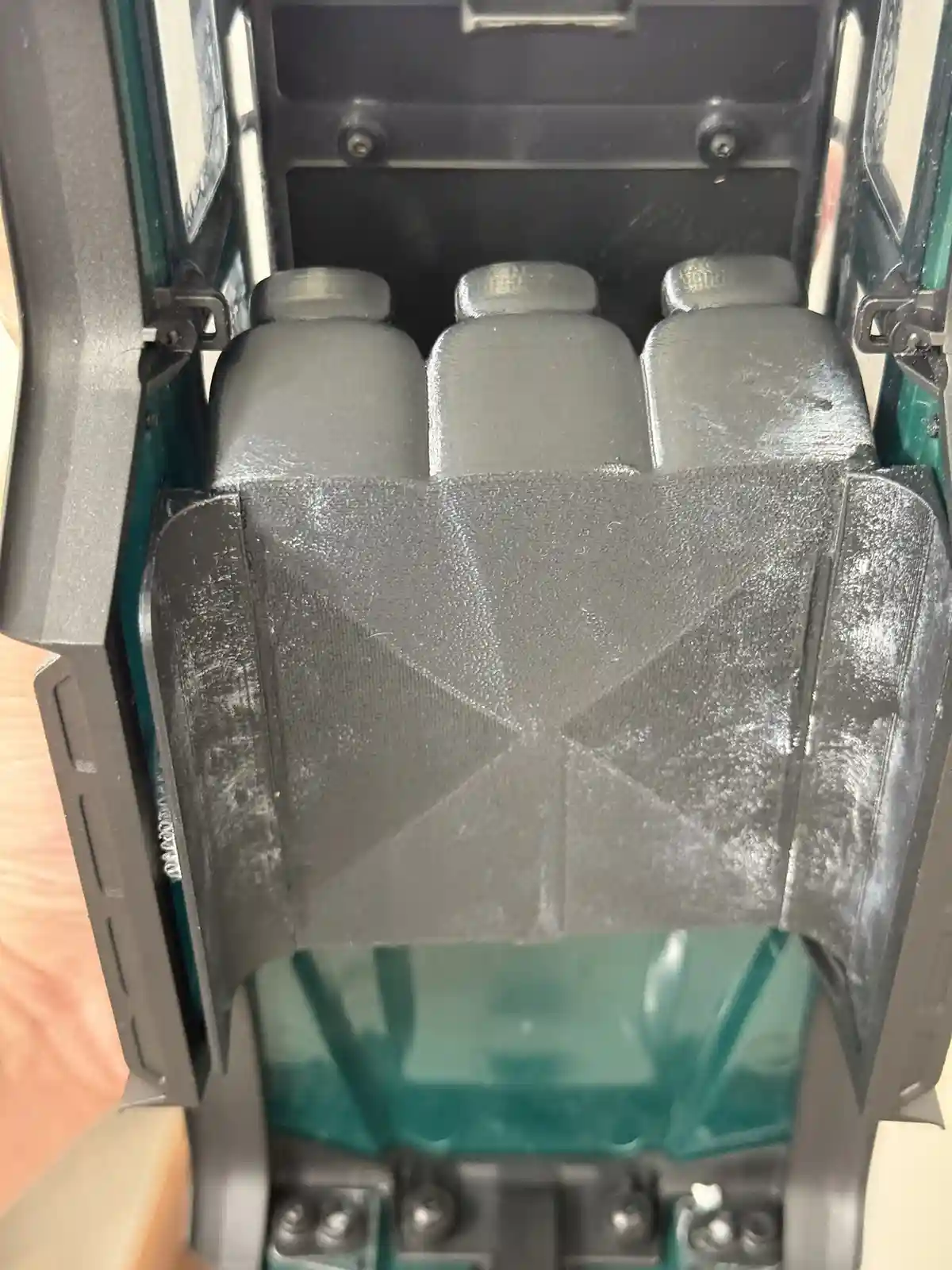 A close-up photo shows the interior of a small green toy car with three gray plastic seats. The floor of the car is covered…