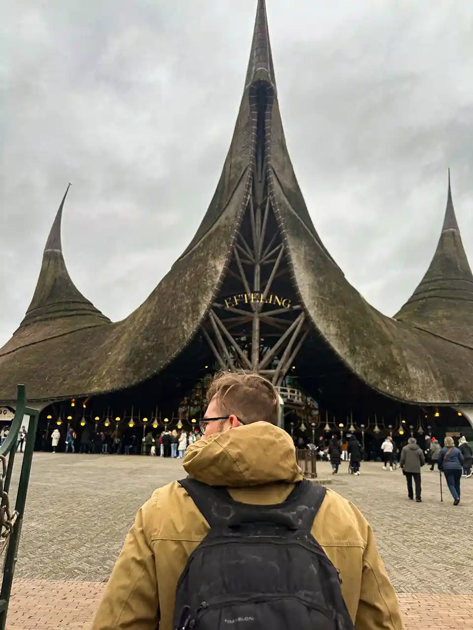 A person in a tan hooded jacket and black backpack stands with their back to the camera, looking up at the distinctive…