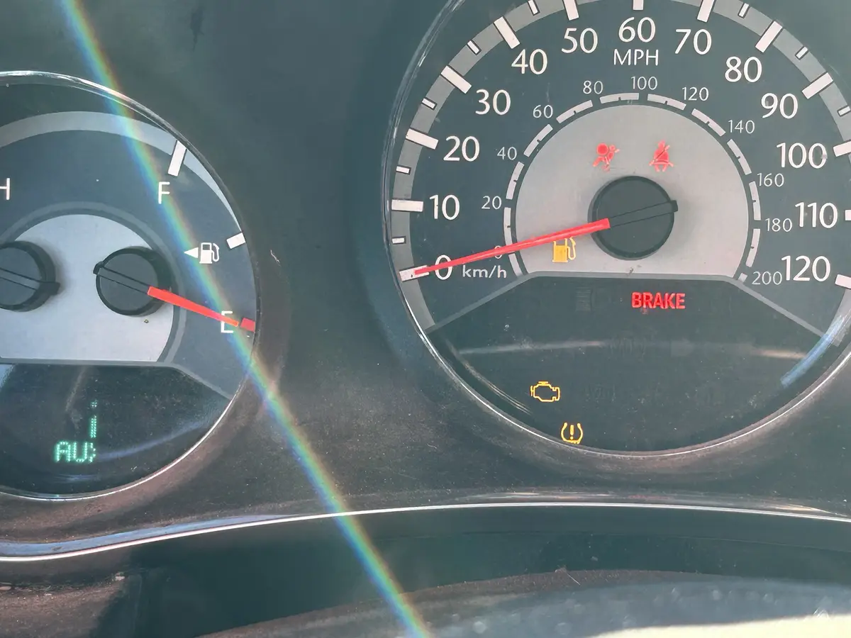 A close-up of a car's dashboard shows the fuel gauge needle pointing at 'E' for empty, the speedometer at 0 km/h, and…
