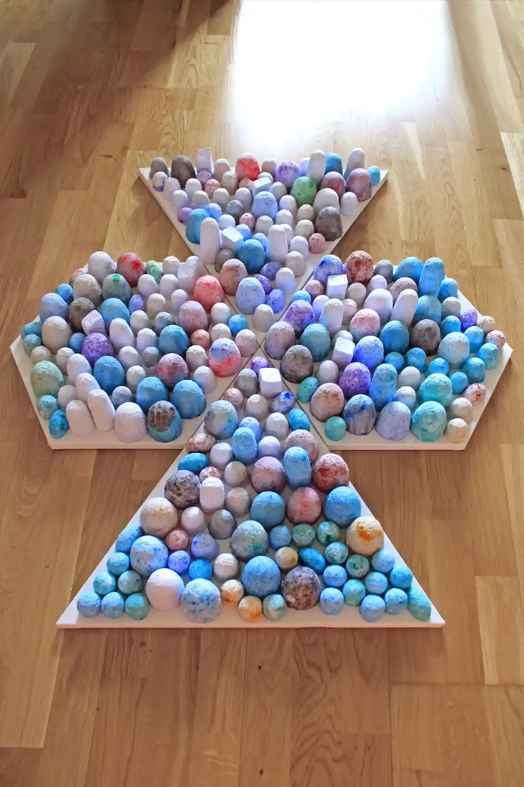 An overhead shot shows four white triangular boards arranged in a diamond shape on a light wood floor, each filled with…