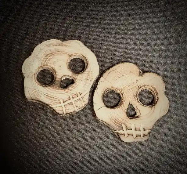 Two hand-carved wooden skull decorations with stitched mouths and dark eye sockets sit side by side on a dark textured…