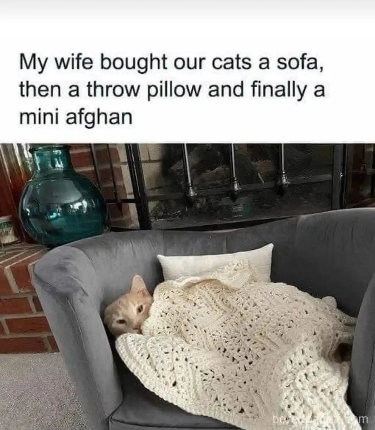 A light orange cat is curled up and sleeping in a small grey armchair, partially covered by a cream-colored crocheted…