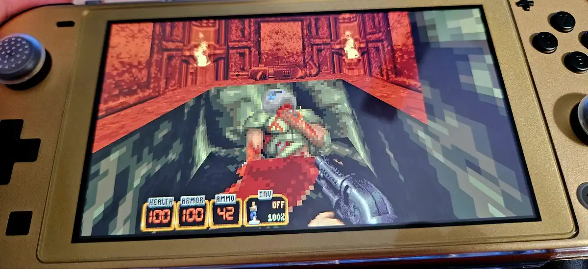 A gold Nintendo Switch console displays a pixelated first-person shooter game, likely a port of Doom, showing a player…