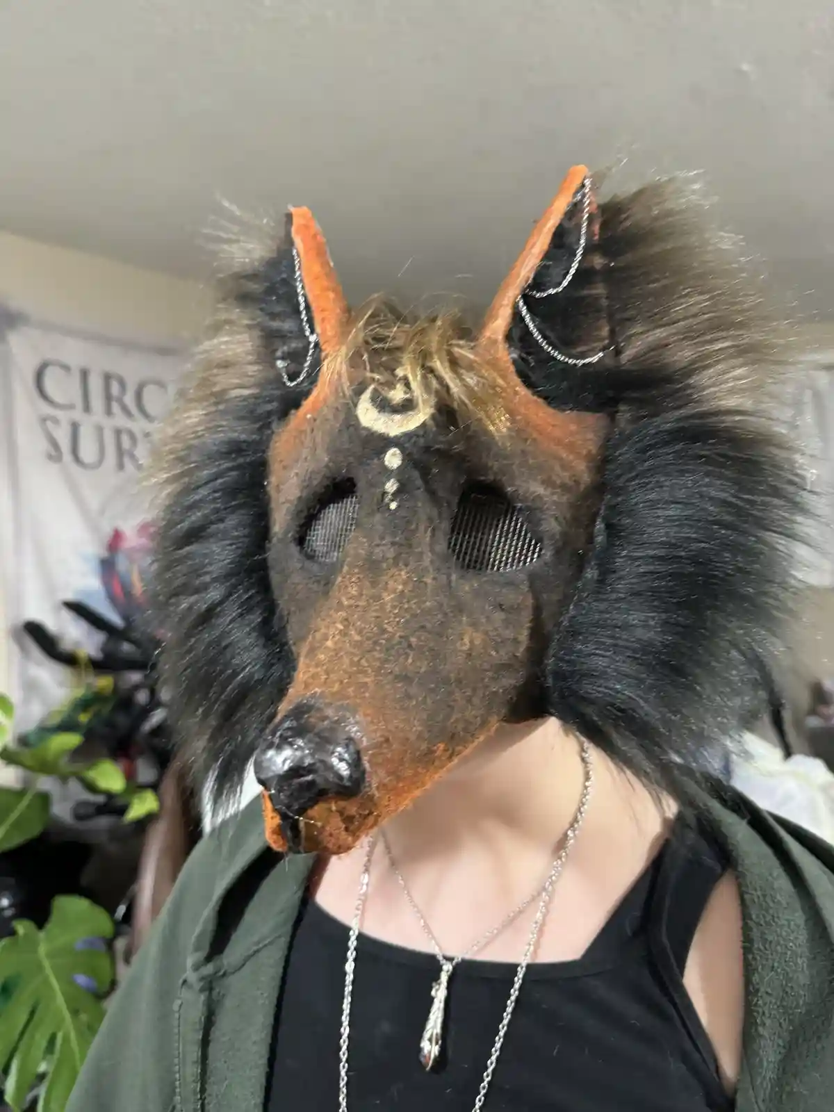 A person wears a detailed, furry wolf mask with orange accents and silver chains on the ears, covering their face except for…