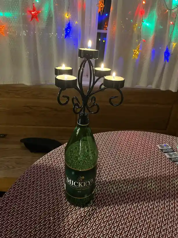 A green bottle of Mickey's Fine Malt Liquor is repurposed as a candle holder, with a black metal candelabra attached to its…
