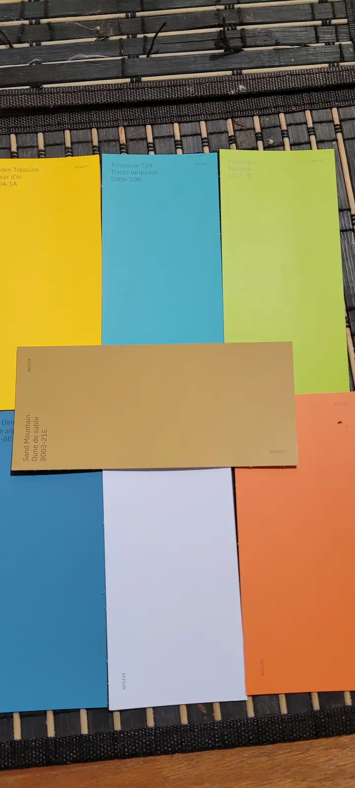 Several paint swatches with names like 'Asparagus', 'Turquoise Tint', and 'Sand Mountain' are arranged on a woven mat. The…